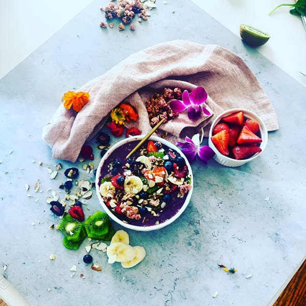 A vibrant acai bowl with fresh fruit, granola, and nuts, alongside a bowl of strawberries.