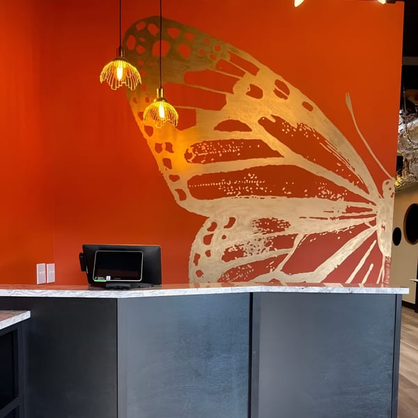 Restaurant counter with a gold butterfly mural on an orange wall and two hanging lights.