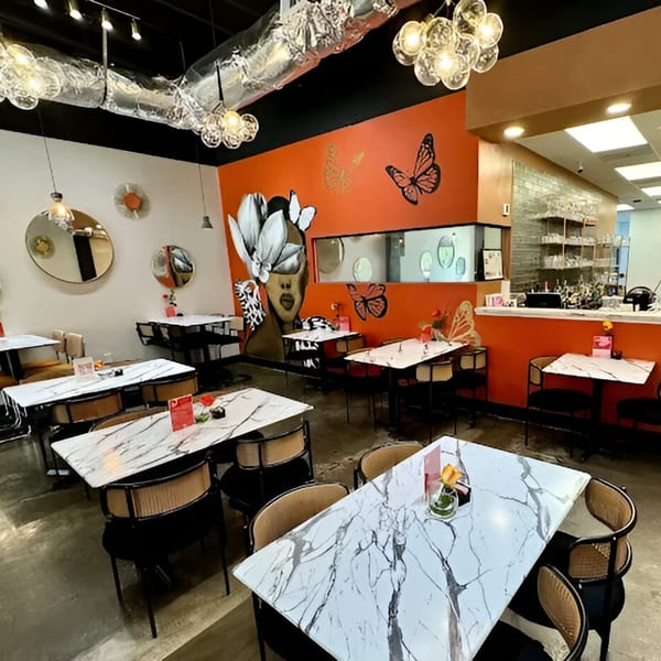 The interior of Scrum-did-dly-ump-tious restaurant with marble tables, modern chairs, and vibrant orange walls.