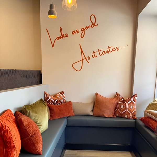 Cozy corner booth with dark blue seating, colorful pillows, and a wall decal reading "Looks as good As it tastes..."