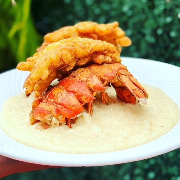 Fried lobster tails and grits on a white plate, with a green leafy background.
