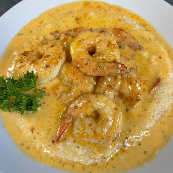Shrimp and grits, a breakfast dish, with a creamy orange sauce and a sprig of parsley.