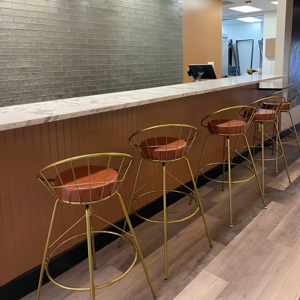 A long marble counter with four gold-framed bar stools with brown leather seats at Scrum-did-dly-ump-tious.